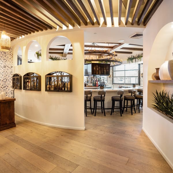 A curved hallway with arched cutouts leads to a bar area with stools and a large chandelier.