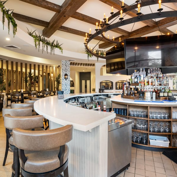 La Cocina's bar area with a white curved counter, brown bar stools, and a large chandelier.