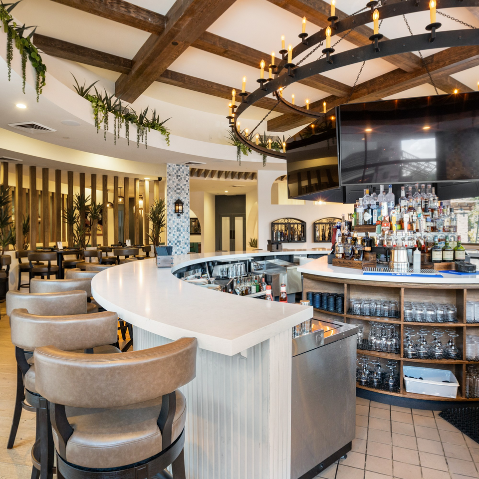 La Cocina's bar area with a white curved counter, brown bar stools, and a large chandelier.