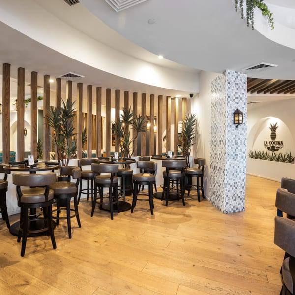 Interior of La Cocina restaurant with high-top tables, bar stools, wooden dividers, and tiled pillars.
