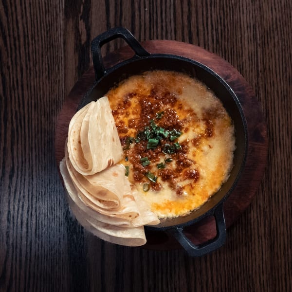 Melted cheese with chorizo and green onions in a cast iron skillet, served with tortillas.