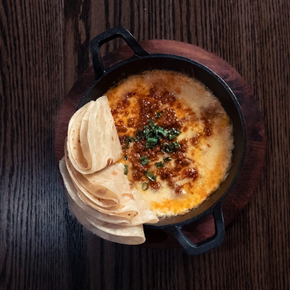 Melted cheese with chorizo and green onions in a cast iron skillet, served with tortillas.