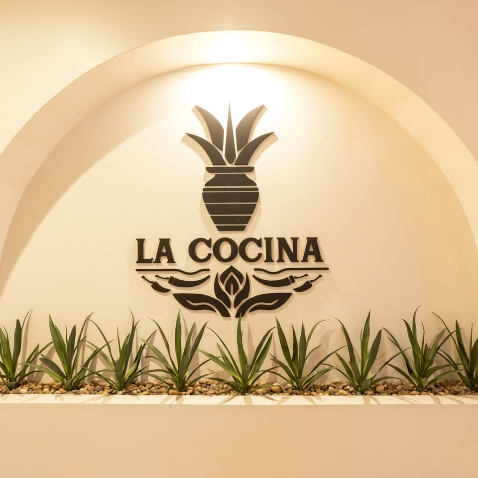 La Cocina restaurant logo, black on a white arched wall, with agave plants below.
