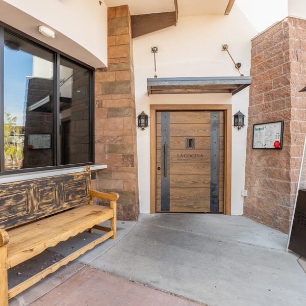 The entrance to La Cocina restaurant, featuring a wooden door, stone walls, and a wooden bench.
