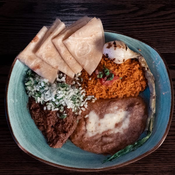 La Cocina's Mexican platter with tortillas, rice, beans, and grilled onion on a blue plate.