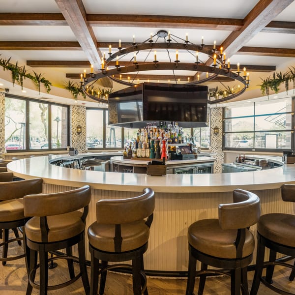 La Cocina's circular bar with brown leather stools, a large chandelier, and bottles of liquor.