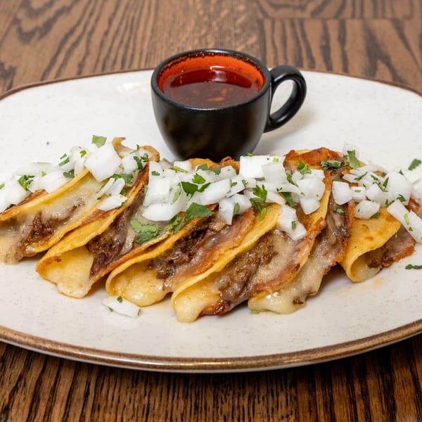 Birria tacos with melted cheese, chopped onions, and cilantro, served with a side of consommé.